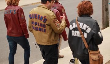 three people wearing Queen's jackets walking on campus