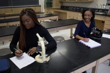 Two female students working in a lab with microscopes in front of them. 